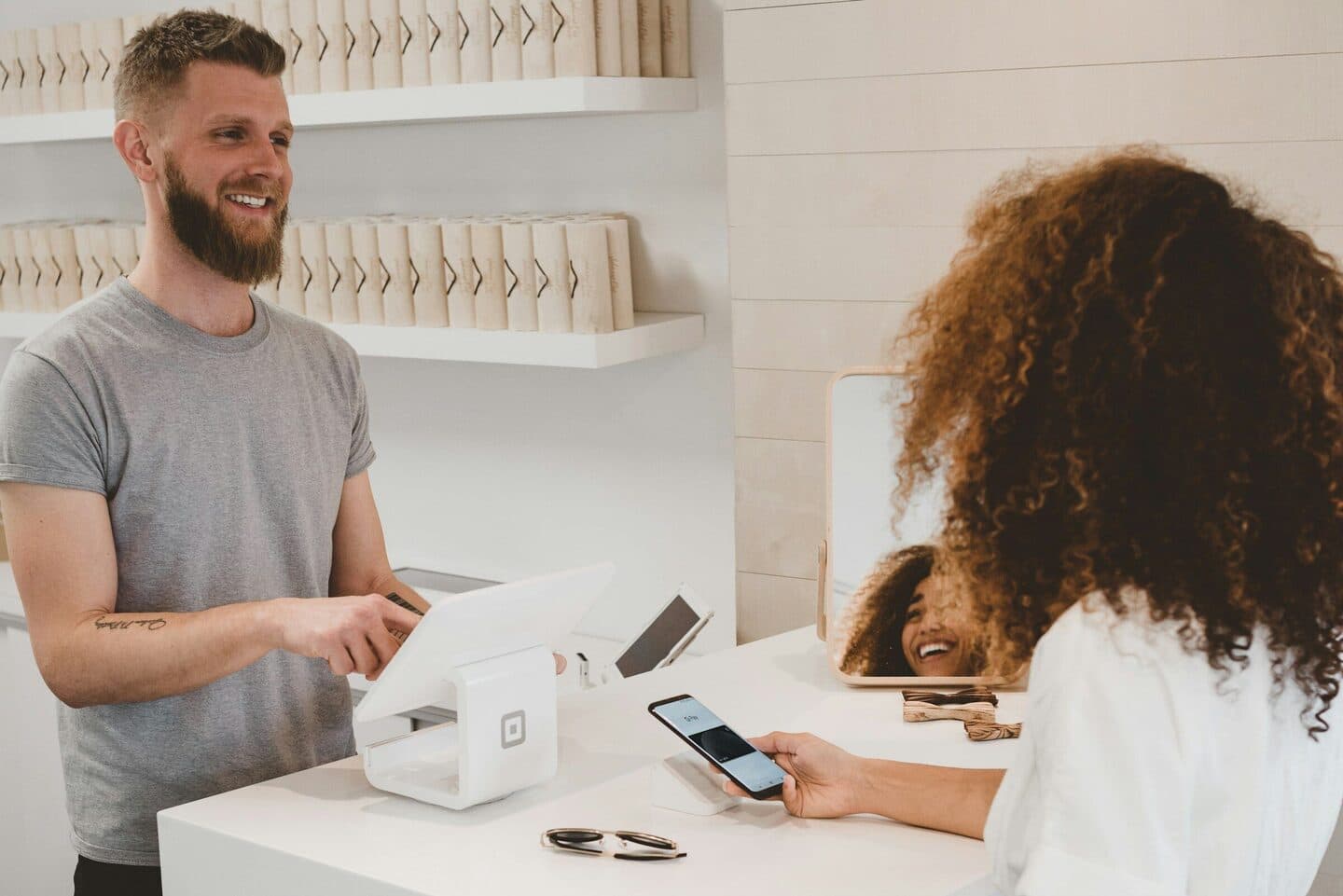 Verkäufer an der Kasse lächelt einer Kundin zu, die mit dem Handy bezahlt