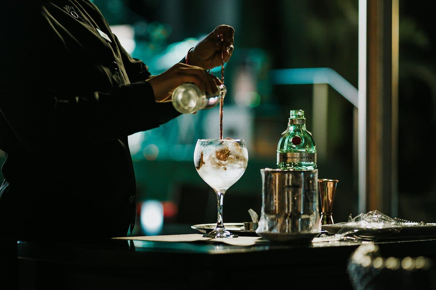 Barkeeper gießt an der Bar einen Drink in ein Weinglas mit Eis